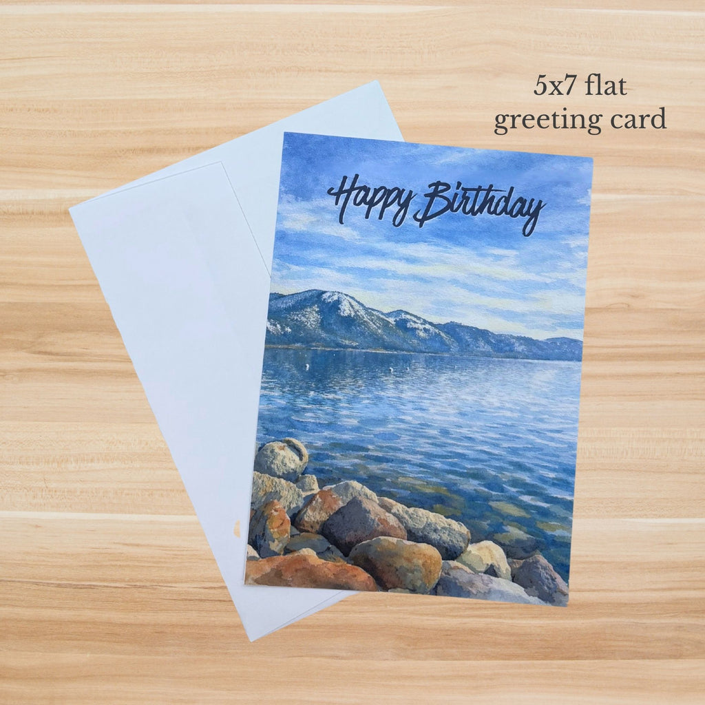 Scenic Lake Tahoe birthday card with blue water, rocky shoreline, mountains, and Happy Birthday text