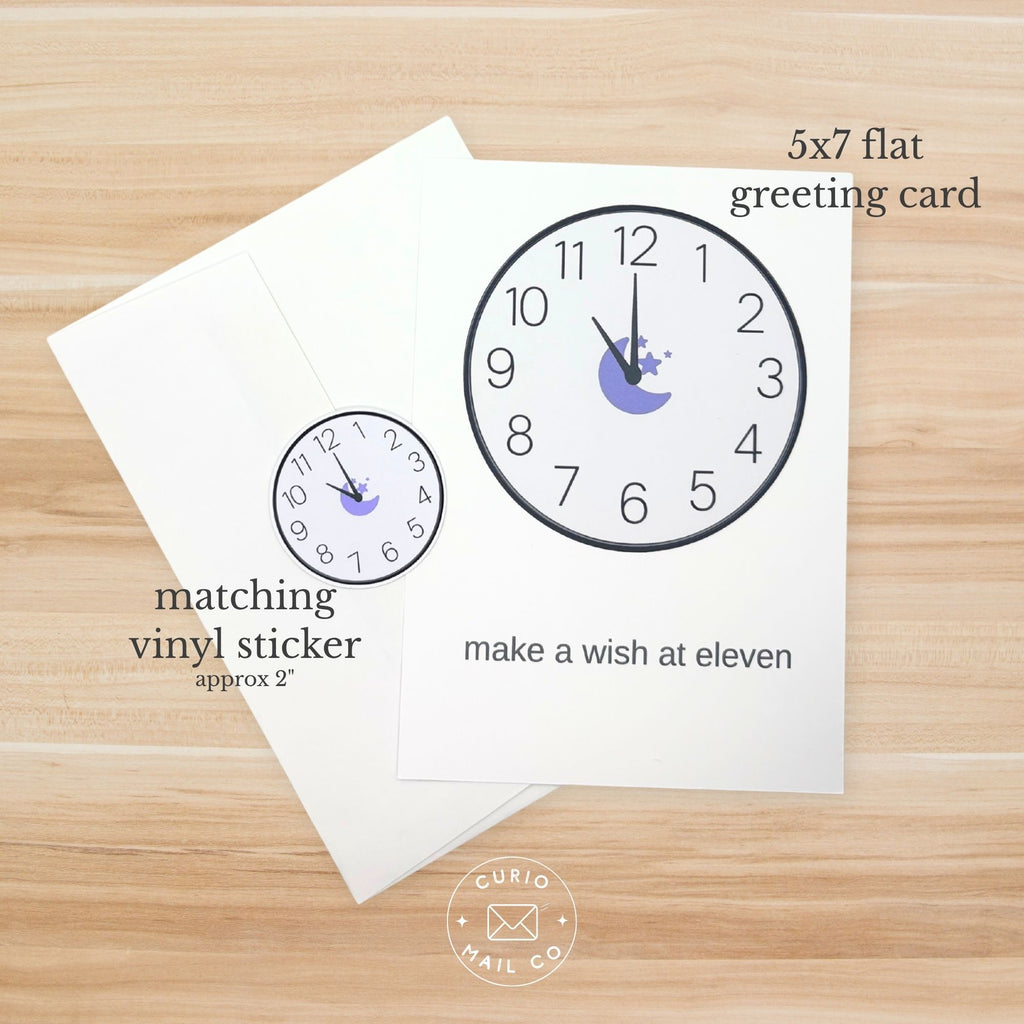 Greeting card with clock design and matching vinyl sticker on a wooden surface, featuring Curio Mail Co branding.