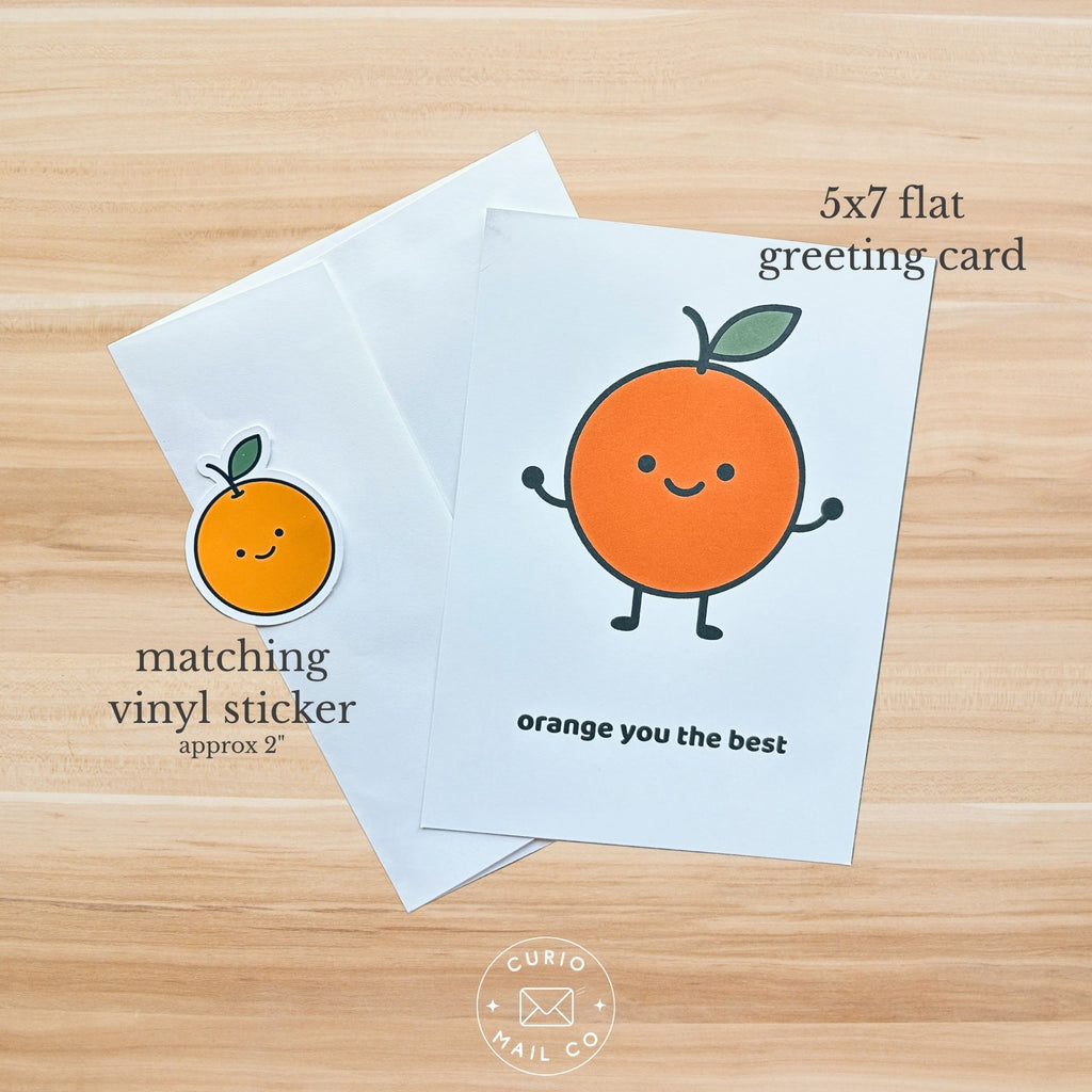 5x7 flat greeting card with a cartoon orange character and matching vinyl sticker on a wooden surface.