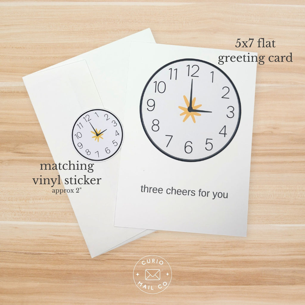 Greeting card with clock design and matching vinyl sticker on a wooden surface, featuring Curio Mail Co branding.