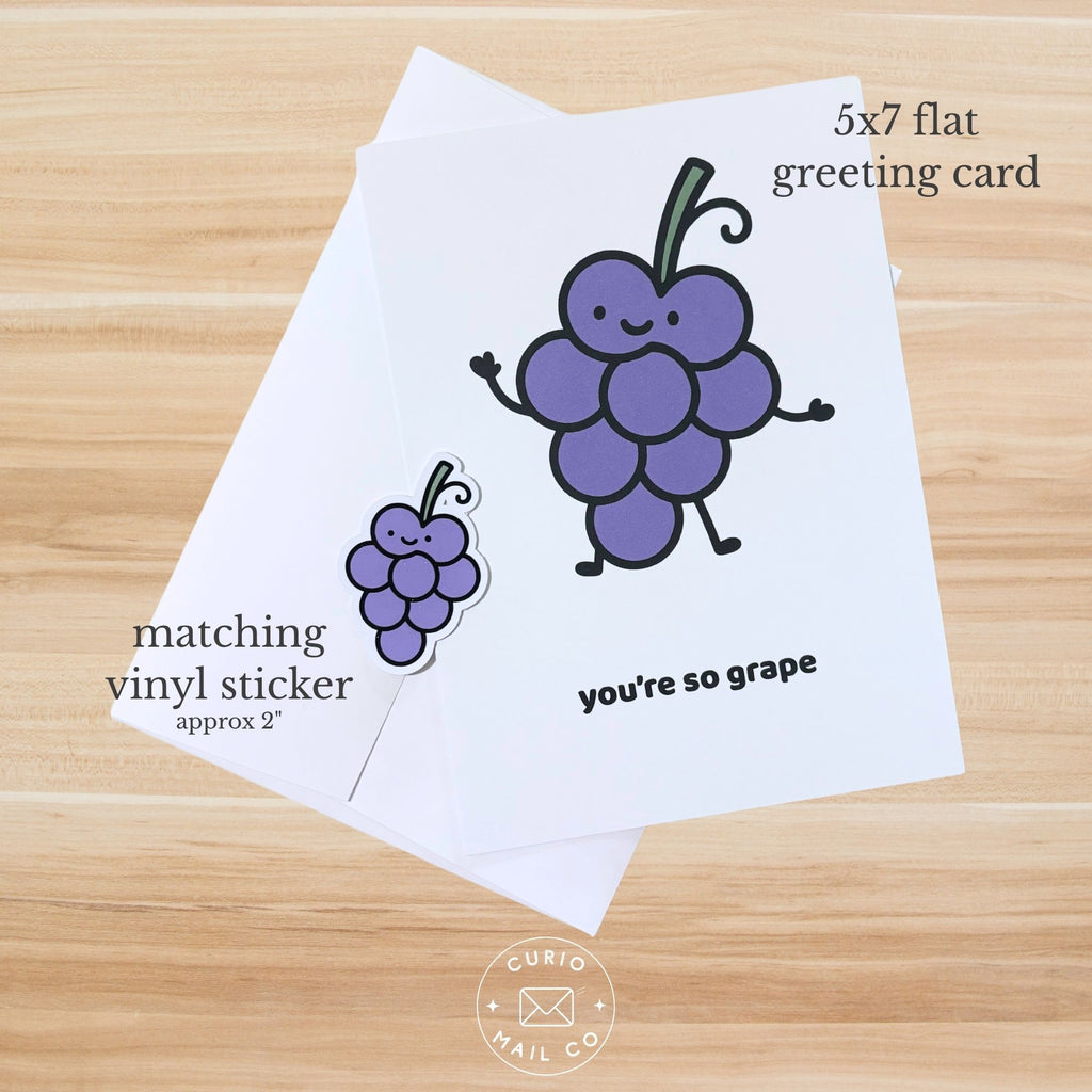 Greeting card with cartoon grapes and matching sticker on a wooden surface